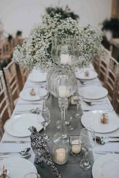 the table is set with white plates, silverware and glass vases filled with baby's breath flowers