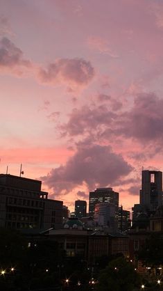 the city skyline is lit up at night with pink clouds in the sky and buildings