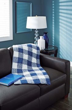 a living room with a couch, table and lamp in the corner that has a blue plaid blanket on it