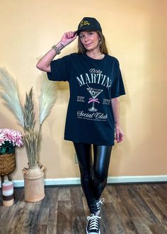 Join the club in style with our Dirty Martini Social Club Graphic Tee. This oversized black tee features a relaxed fit, complete with a classic crew neckline, short sleeves, and a straight hem for effortless comfort. The standout design includes "Dirty Martini Social Club" lettering alongside a playful martini glass graphic with a pink croquette ribbon. This tee offers both style and comfort, perfect for your next casual outing or social event. Oversized fit Crew neckline Short sleeves Straight Crew Neck T-shirt With Letter Print For Night Out, Letter Print Crew Neck T-shirt For Night Out, Oversized Short Sleeve Tops For Night Out, Graphic Print Short Sleeve T-shirt For Night Out, Black Crew Neck T-shirt For Night Out, Black Graphic Print T-shirt For Night Out, Casual Crew Neck T-shirt For Night Out, Graphic Tee Crew Neck T-shirt For Night Out, Graphic Tee With Crew Neck For Night Out