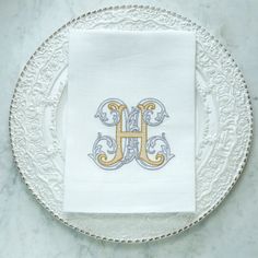 the monogrammed napkin is on top of a white plate with silver trimming