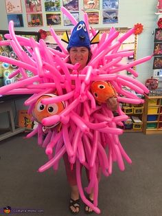 a woman in a blue hat is holding pink balloons with cartoon characters on them and smiling