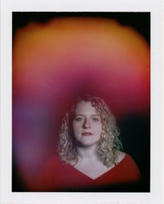 a woman with curly hair wearing a red shirt and posing for a photo in front of an abstract background