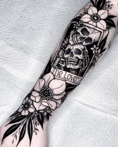 a black and white tattoo on the arm with flowers, skull and crossbones