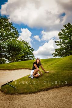 a woman sitting on top of a lush green field next to a golf course with trees