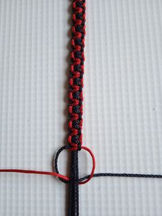 a red and black piece of string on top of a white sheet with a knot