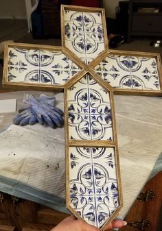 a hand holding up a cross made out of tile on top of a wooden table