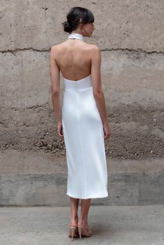 a woman standing in front of a stone wall wearing a white dress and high heels