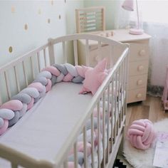 a white crib with pink and grey pillows on it