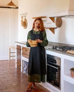 a woman standing in a kitchen holding a paper bag and looking at the oven door