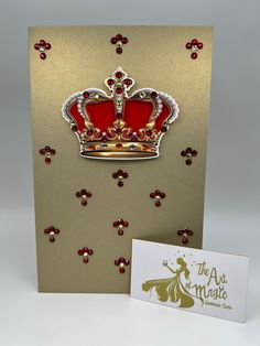 a gold and red card with a crown on it next to a white greeting card