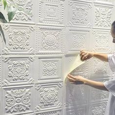 a woman is working on a wall with white paint and decorative plaster tiles in front of her