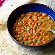 a blue bowl filled with beans on top of a white cloth next to a spoon