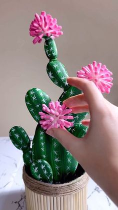 a hand holding a fake cactus with pink flowers