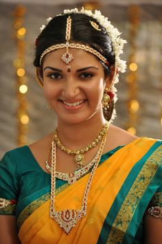 a woman in a yellow and green sari with jewelry on her head, smiling at the camera