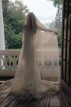 a woman in a wedding dress is standing on a porch with her veil over her head