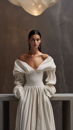 a woman in a white dress standing next to a light fixture with her hands on her hips