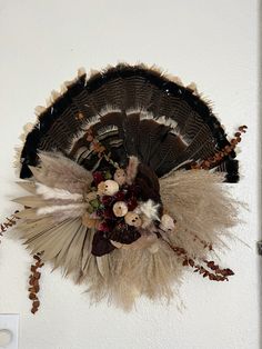 a decorative wall hanging with feathers and flowers on it's side, against a white wall