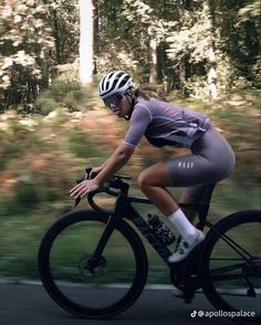 a woman riding a bike down a street next to trees and grass in the background