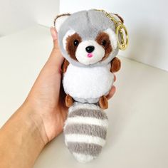 a hand holding a stuffed animal keychain with a raccoon on it