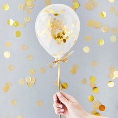 a person holding a white balloon with gold confetti on it's tail