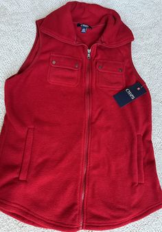 Add some warmth to your outfit with this stylish Chaps vest. The vibrant red color gives a pop of color to any look. Made with a cozy fleece fabric, this mid-length vest features a full front zipper and pockets for convenience. Perfect for travel or casual wear, this sleeveless vest is machine washable and easy to care for. The solid pattern and classic theme make it a timeless addition to any wardrobe. Available in size M, this Chaps vest is a regular fit and is ideal for layering in the fall, winter, or spring. Please ask if you have any questions - 275 Casual Red Sweater Vest For Winter, Casual Fleece Vest For Winter, Casual Winter Fleece Vest, Casual Red Vest With Pockets, Casual Fleece Vest With Pockets, Classic Theme, Fleece Vest, Sleeveless Vest, In The Fall