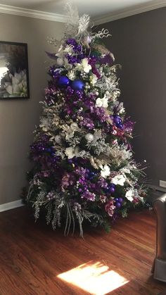 a decorated christmas tree with purple and white flowers in the corner of a living room