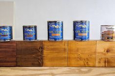 five cans of canned food are lined up on a wooden shelf