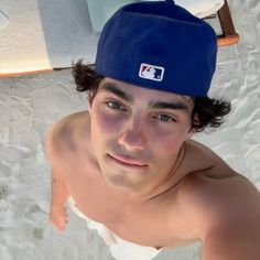 a man wearing a baseball cap on top of his head while sitting in the sand