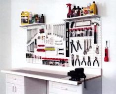 a white workbench with tools hanging on it's wall and cabinets below