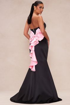 a woman wearing a black and pink dress with a large bow on the back of it