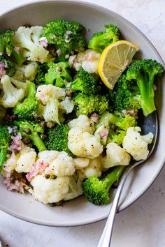 a bowl filled with broccoli, cauliflower and lemon wedges next to a spoon