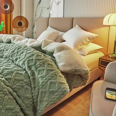 a bed with green comforter and pillows in a bedroom next to a chair, lamp and window