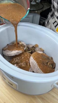 someone pouring sauce into a slow cooker filled with meat and mushroom patties in it