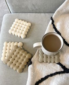 two cookies and a cup of coffee on a blanket next to a couch with a white towel