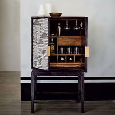 an open cabinet with bottles and glasses in it on the floor next to a wall