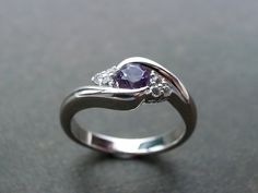 The 2.3 mm band is made from shiny, 14K white gold and curves lovingly around a sparkling, richly colored amethyst center stone. The three round white sapphires on either side of the amethyst add a unique finishing touch of texture and brilliance. Specifications: 4mm round brilliant cut natural Amethyst  6 Round Brilliant cut natural White Sapphire 14K white gold  Ring Width: 2.3mm Currently made to order pieces may take up to 10-15 business days to complete, or let me know if you need it urgent Elegant White Gold Amethyst Ring With Polished Finish, Fine Jewelry Platinum Amethyst Wedding Ring, Amethyst Wedding Ring With Polished Finish, Wedding Amethyst Ring With Polished Finish, Elegant 14k White Gold Purple Ring, Elegant White Gold Amethyst Promise Ring, Elegant Purple 14k White Gold Ring, White Gold Amethyst Ring With Brilliant Cut For Promise, Fine Jewelry Amethyst Ring With Polished Finish