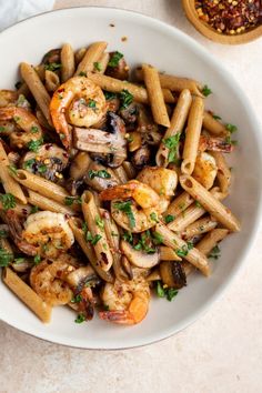 pasta with shrimp, mushrooms and parsley in a white bowl on a marble table