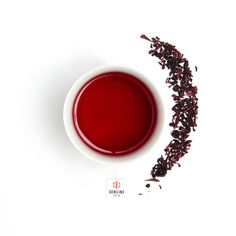 a cup filled with red tea next to a pile of dried blackberries on a white surface