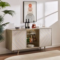 a sideboard with wine bottles and glasses on it in a room next to a potted plant