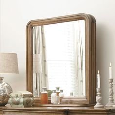 a mirror sitting on top of a wooden dresser next to a lamp and vases