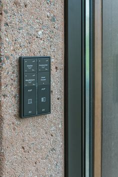 a black control panel on the side of a stone wall next to a glass door