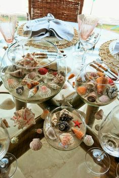 there are many seashells in the glass bowls on the table with wine glasses