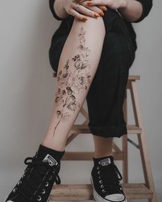 a woman sitting on a stool with her legs crossed and flowers tattooed on the leg