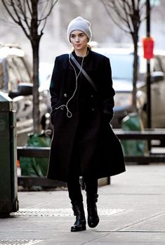 a woman walking down the street with headphones in her ears and wearing a black coat