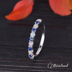 a white gold ring with blue and white stones on it, sitting next to a flower