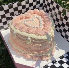 a pink heart shaped cake sitting on top of a checkered tablecloth covered box