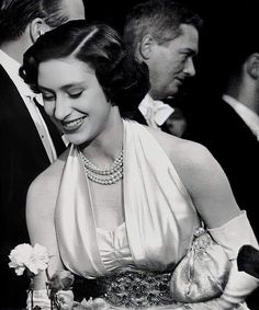 an old photo of a woman in a dress and pearls on her head, smiling at the camera