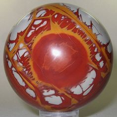 a red and white ball with orange swirls on the top is sitting on a clear base