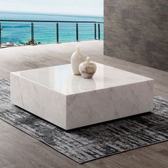 a white marble coffee table with two vases on it in front of the ocean